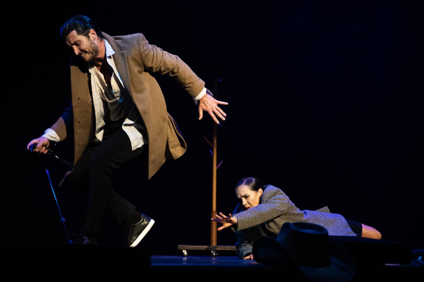 In a suit jacket, Maks walks away as Alexis holds onto his leg to stop him