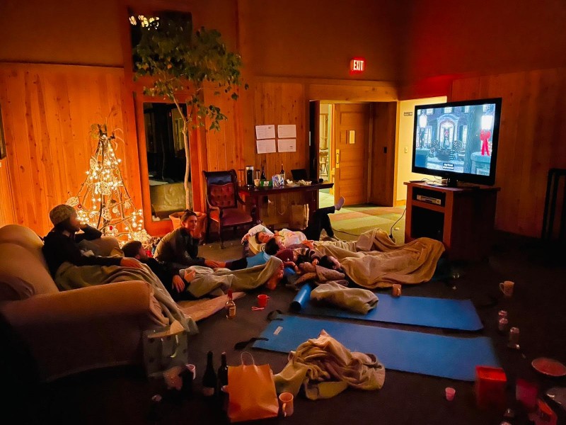 dancers lying on floor watching tv while one sits in chair a lighted twig christmas tree created by dancers brightens the wood paneled den