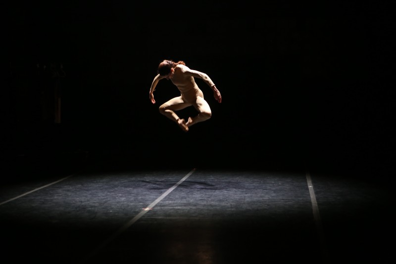 Jaqlin Medlock in a light colored unitard hovers in mid air,her toes touching and the shape of her legs in the air resemble a diamond