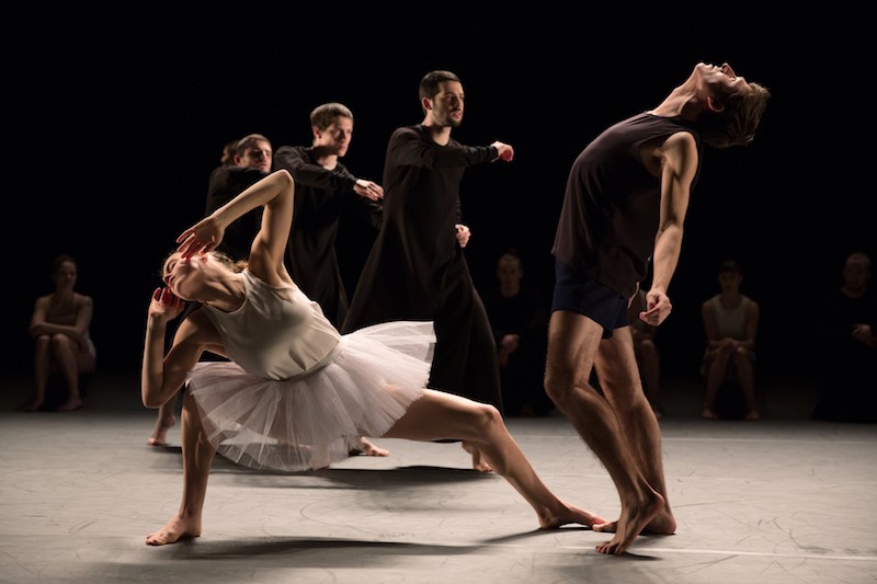 One dancer in a white tutu assumes a deep second position. Her fingertips graze her cheeks. A dancer in black shorts and shirt luxuriates in a back bend.