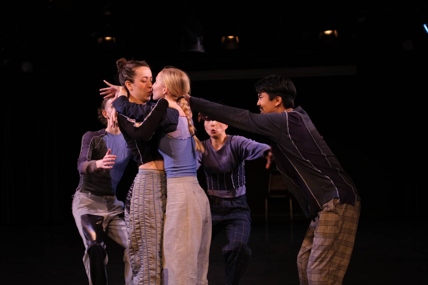 Two women kiss as the other performers look on and react with surprise.
