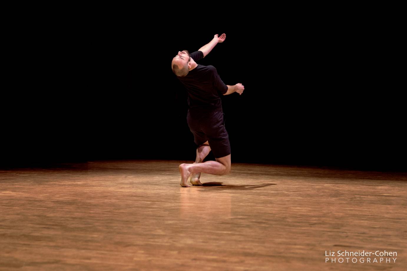 Male dancer in black kneels as he beseeches the heavens.