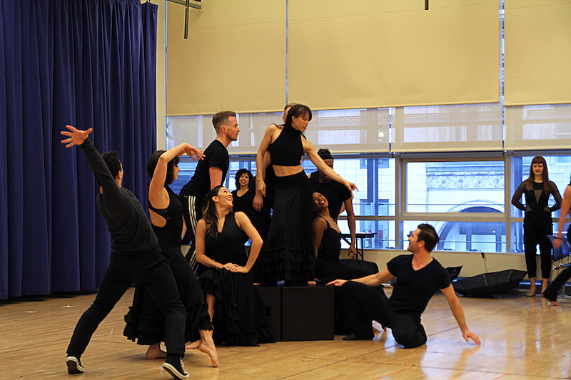 The ADM chorus dressed all in black strike dynamic poses as they huddle together