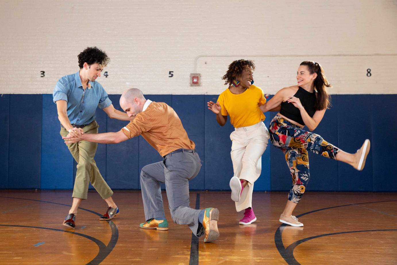 Two same-gender couples swing dance in brightly colored clothing