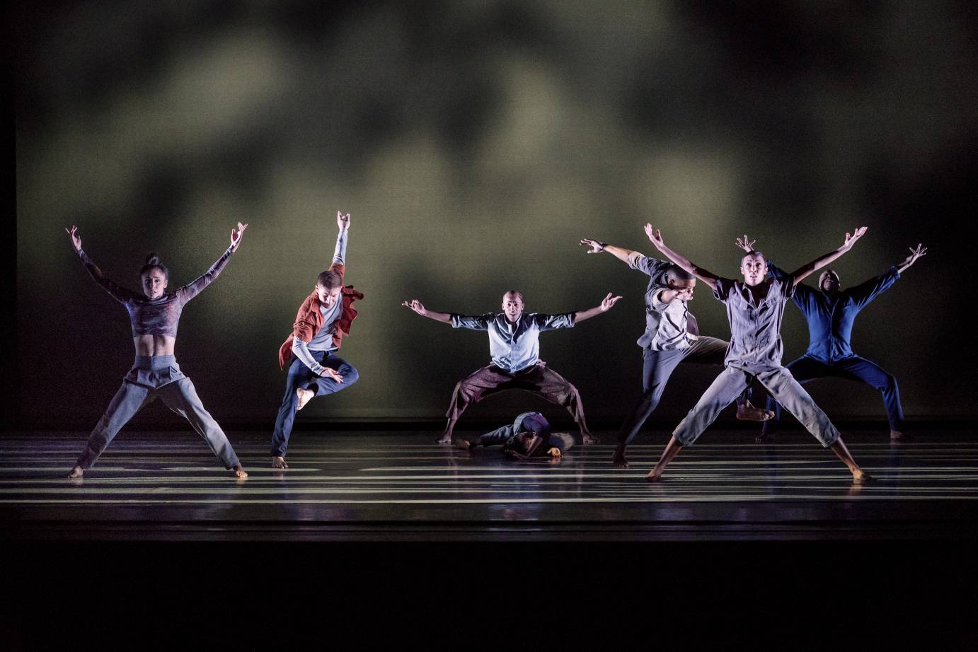 Dancers hold their hand to the sky while one dancers slaps his leg