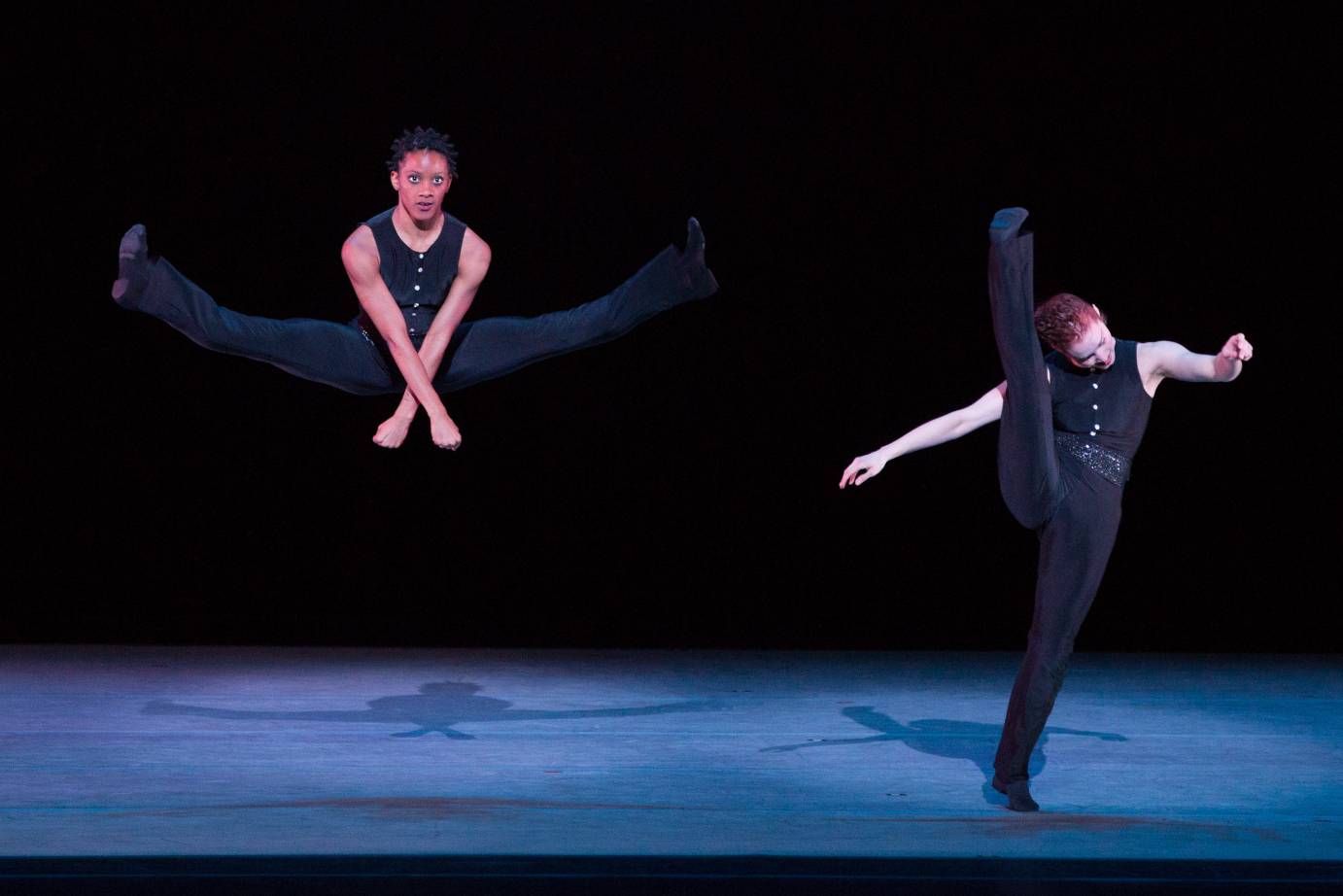 One dancer is in a huge side split jump while another kicks her head