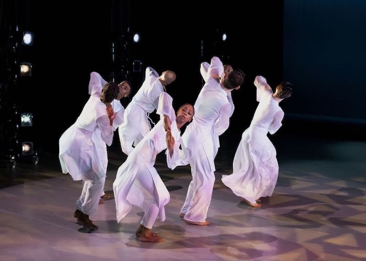 dancers in white flowing robes pose 
