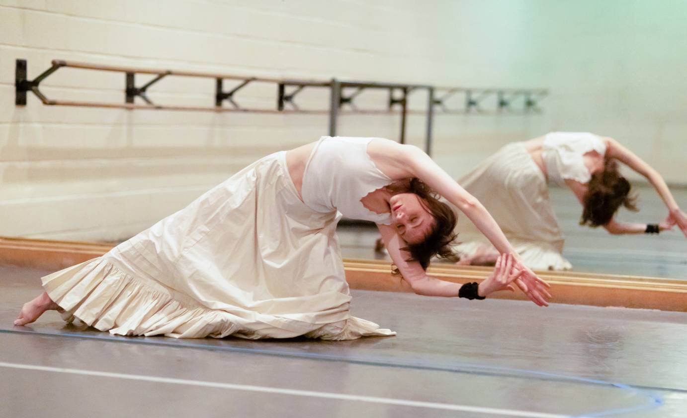 alison in studio on knees bent to side wearing all white rehearsal clothes 