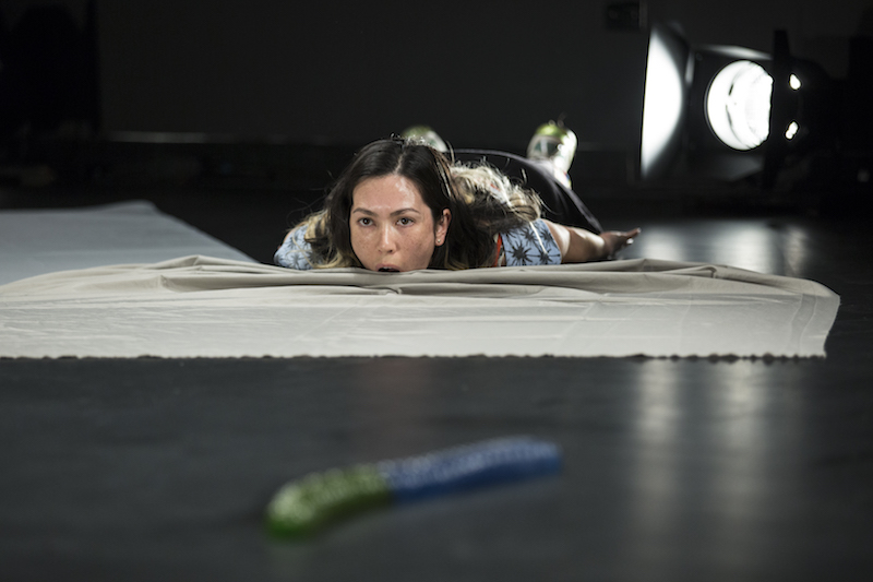 Angela Goh lays on her stomach and opens her mouth as she's about to take a bite of the cloth in front of her.