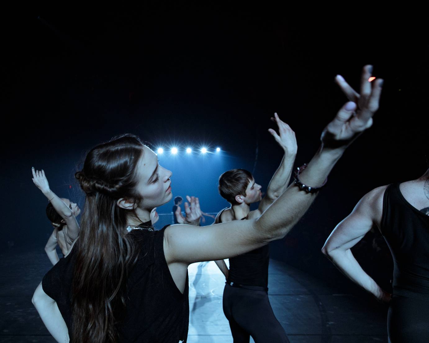 A group of dancers' head and softly bent raised arms bend to the right.
