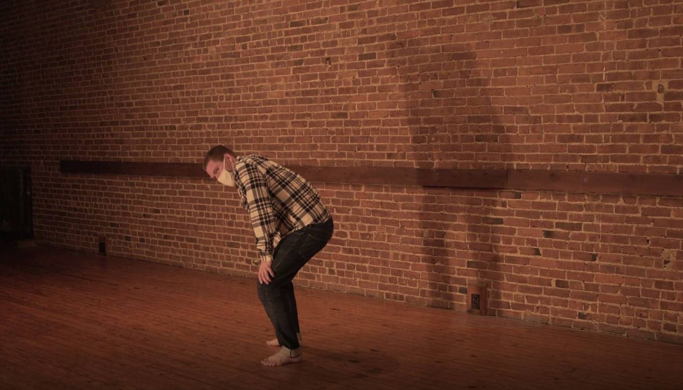 In a flannel shirt, Peter Farrow hunches his shoulders against a brick wall