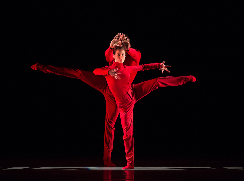 Two dancers in head-to-toe red. They balance on one leg.