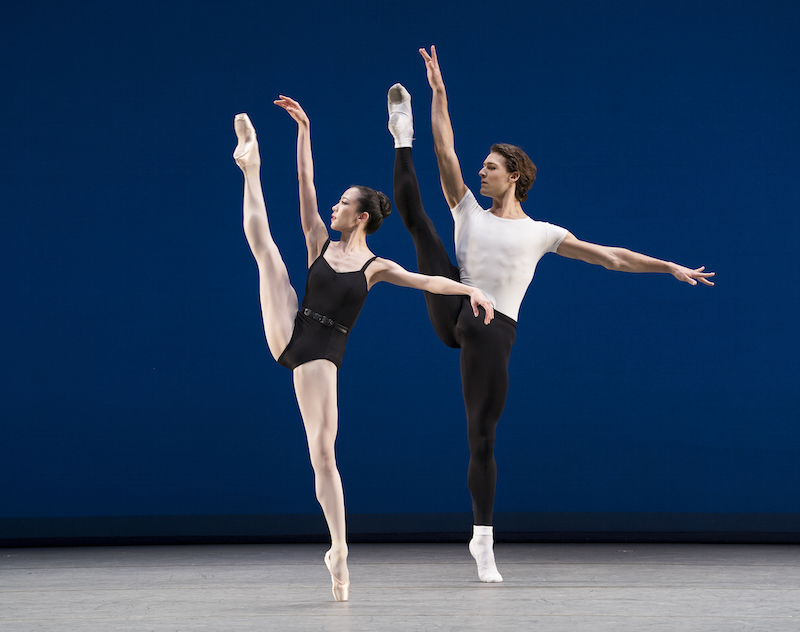 Two dancer extend their legs in a high developpe. They both wear practice-looking clothes: black leotard for Sae-Eun Park and Hugo Marchand wears a white tee and black tights.