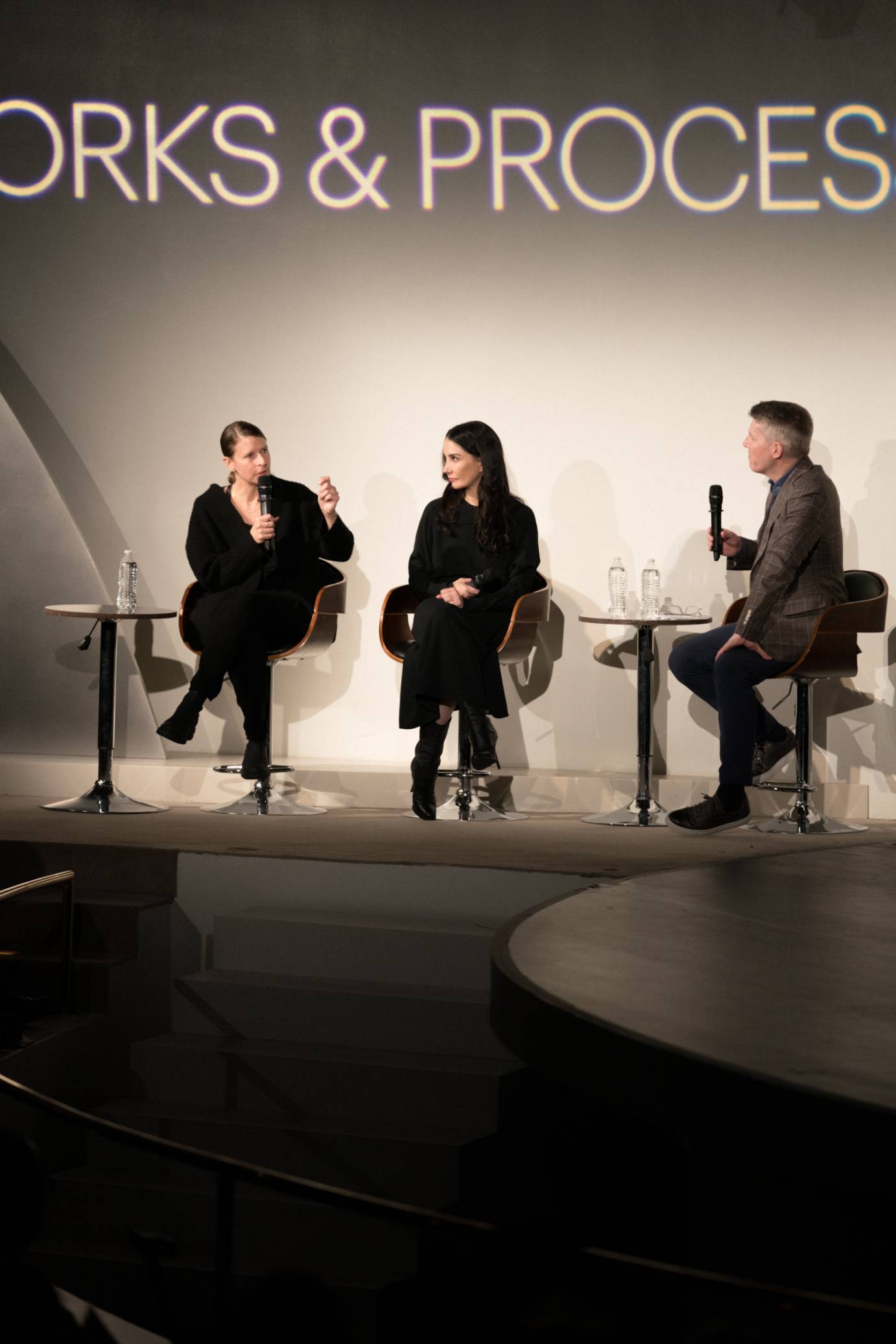 3 people sitting in chairs being interviewed under a works and process sign