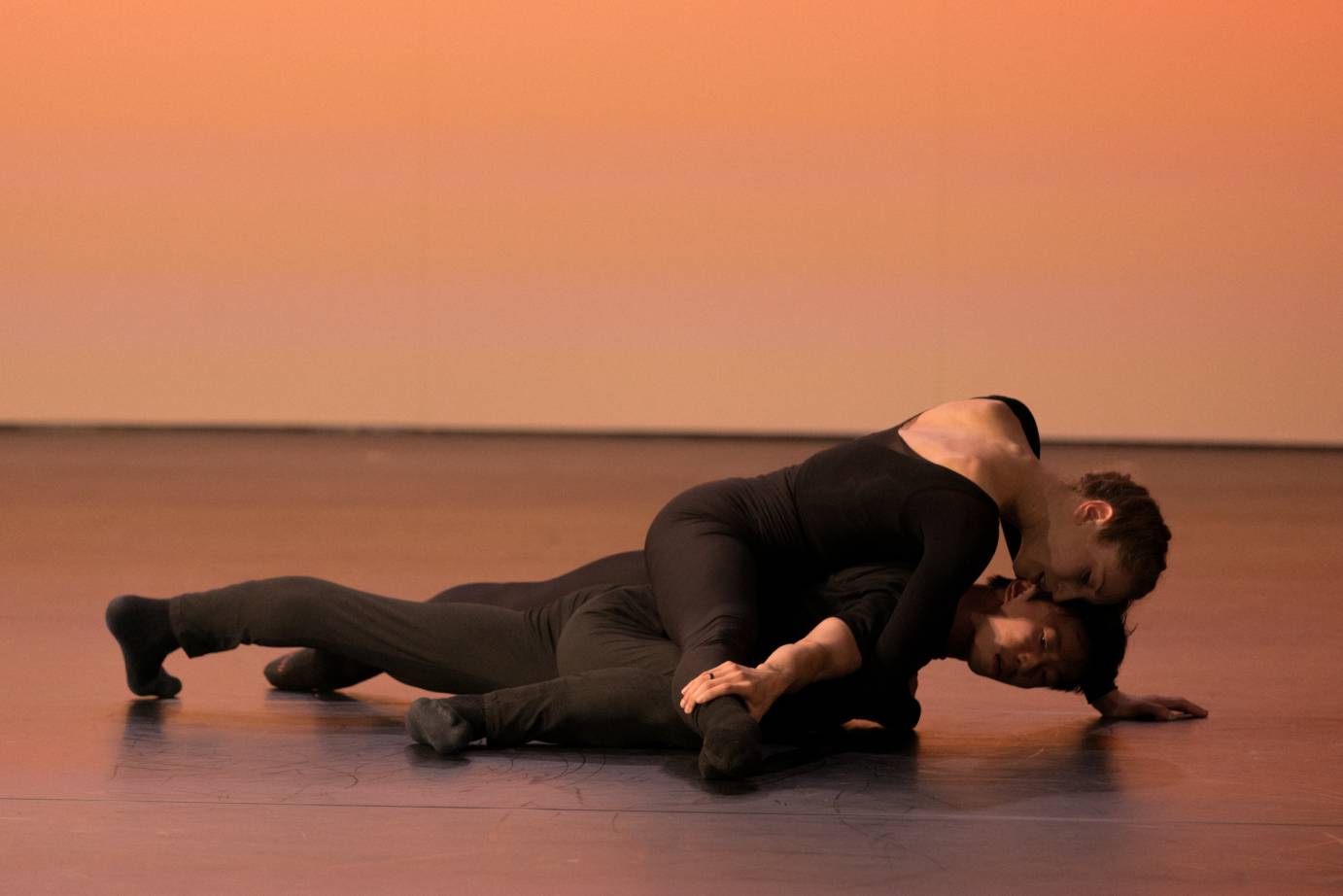 2 dancers lying on the ground, one over the other, leg extended to the side