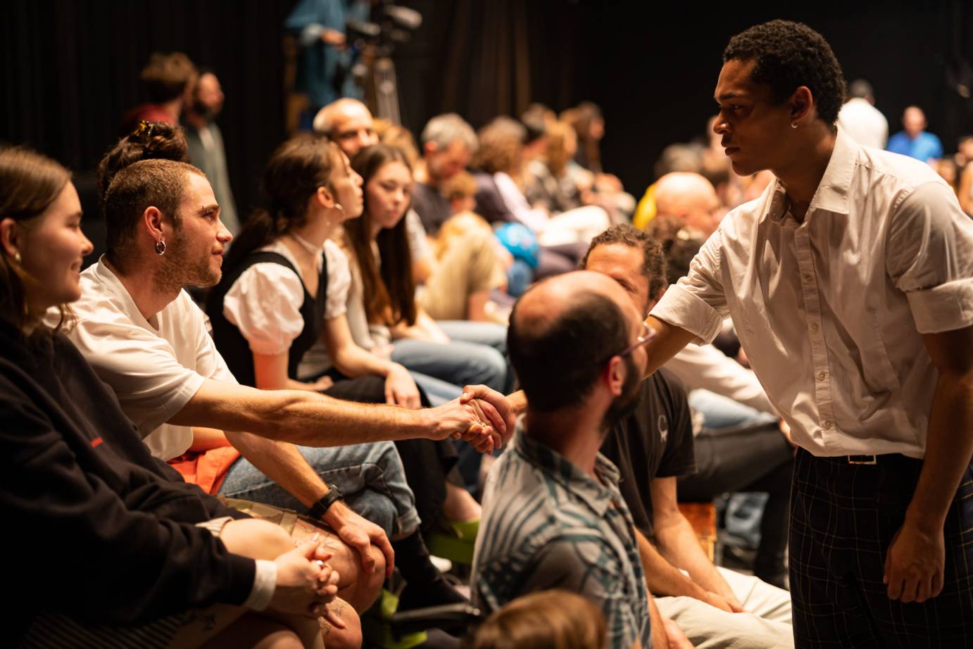 Dancer reaching into audience holding the hand of an audience member as they look into each others eyes
