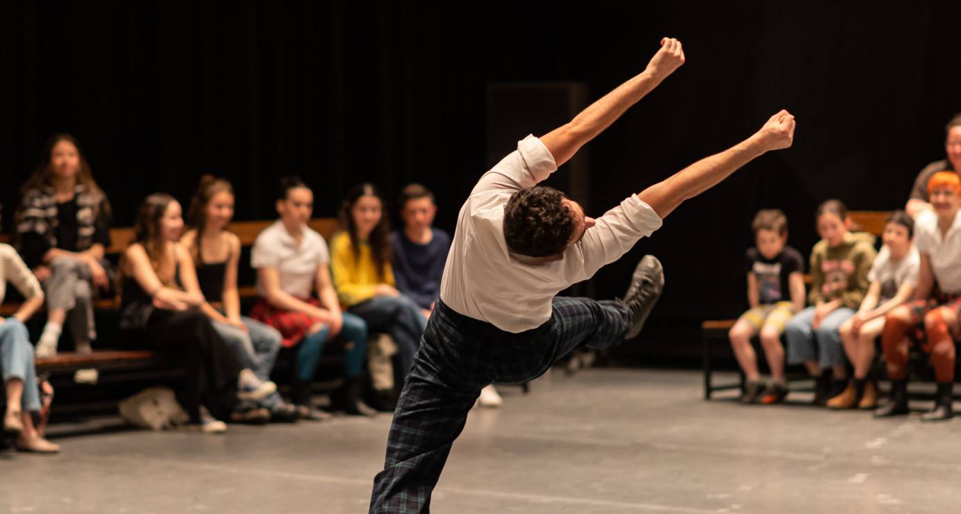dancer in a sideways falling shape, one leg extended and arms raised to sky