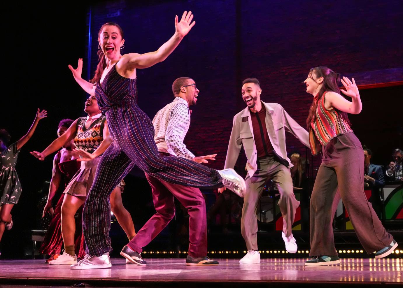 Dancer in foregroun arms outstretched and back leg bent in low attitude shape; dancers in background doing lindy hop