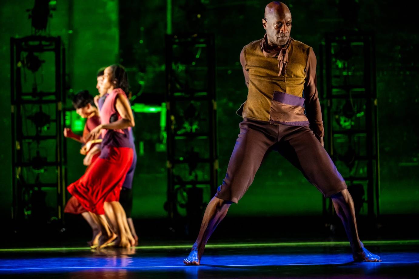 male dancer in a wide stance in the foreground. in background row of females facing side