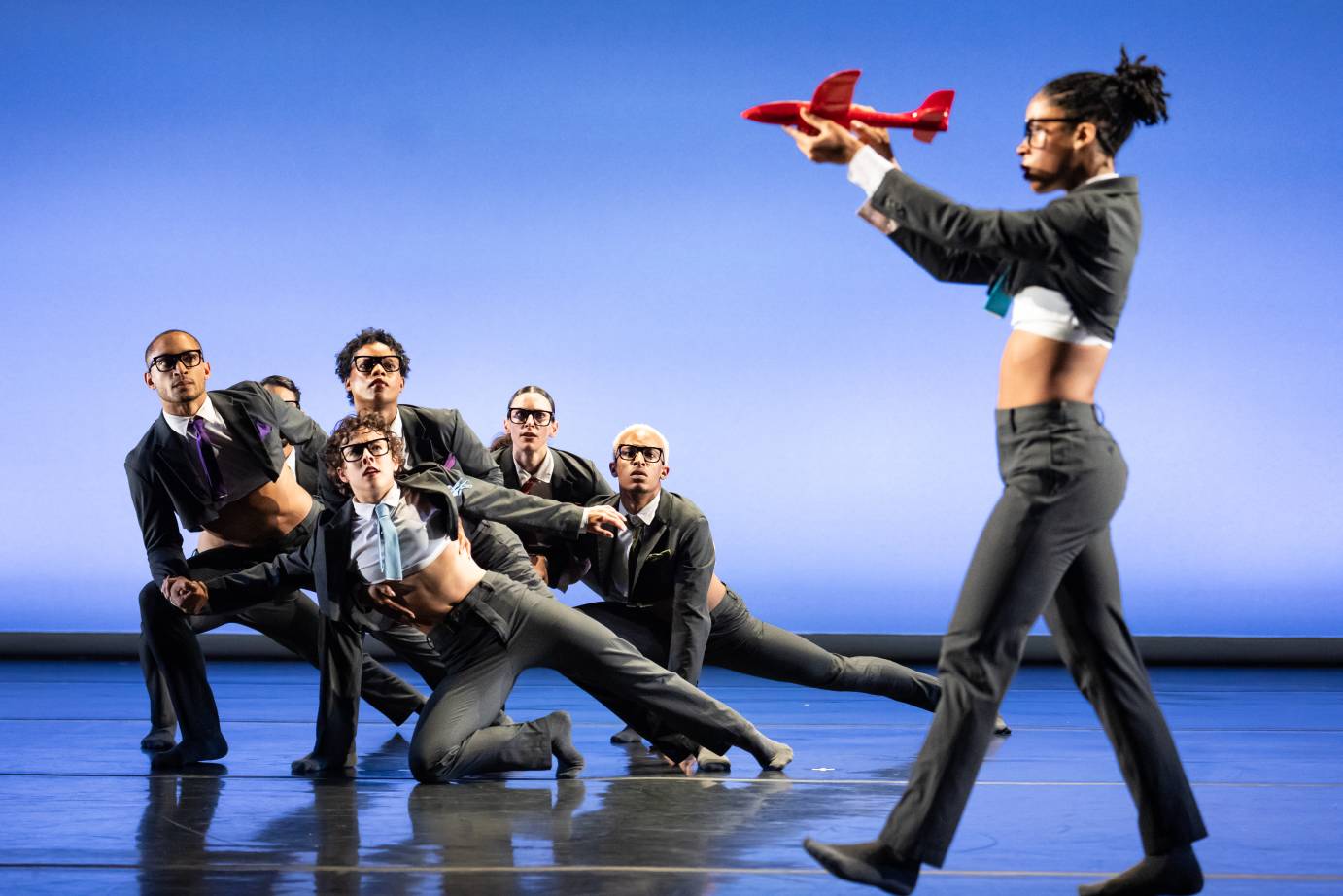 Dancers in low clump upstage. Dance in foreground holding red toy airplane