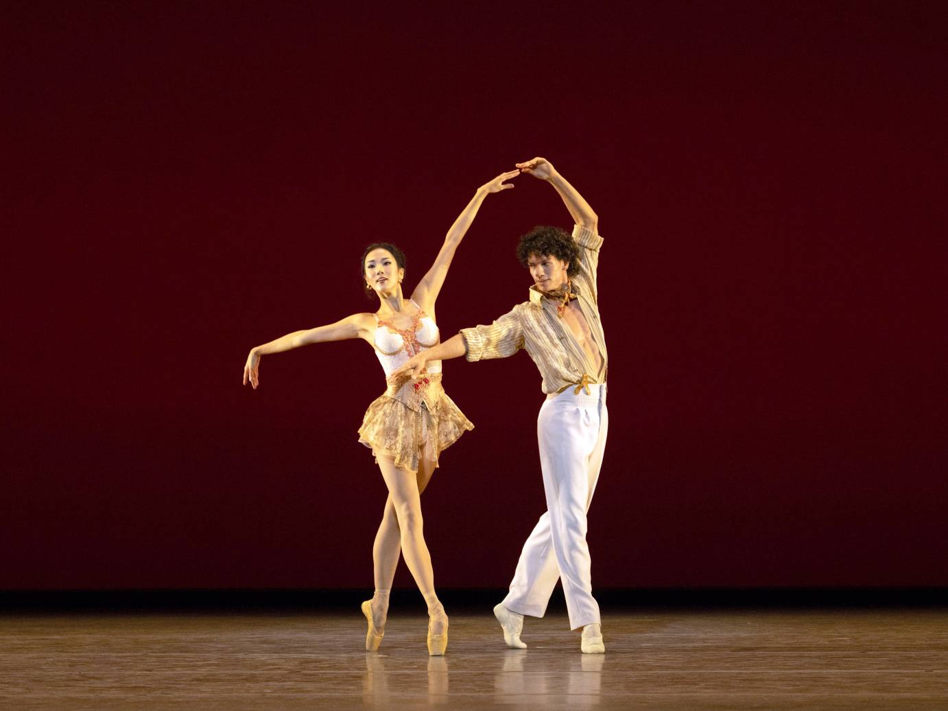 2 dancers. Female in 4th position on pointe, man holding her arm that is up 