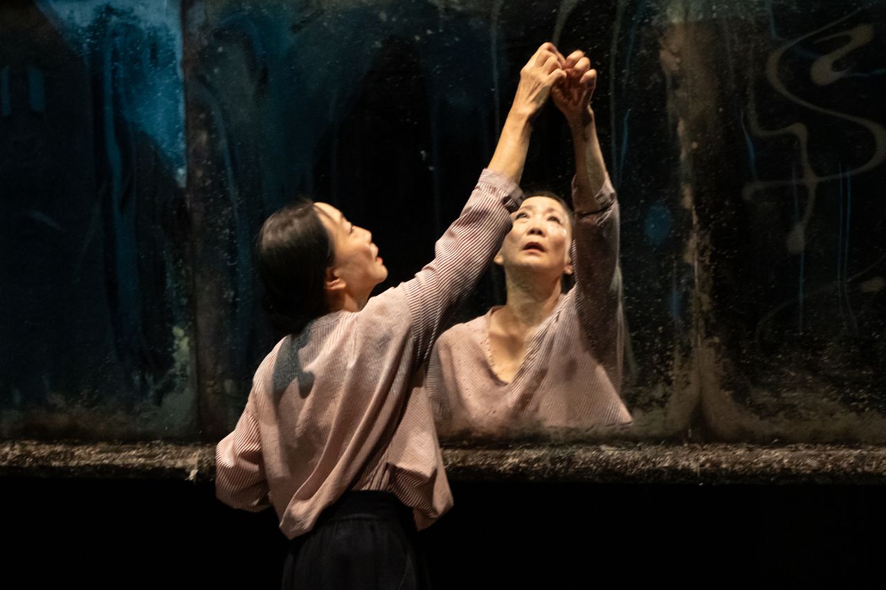 female dancer reaches up to touch her hands reflection in a mirror