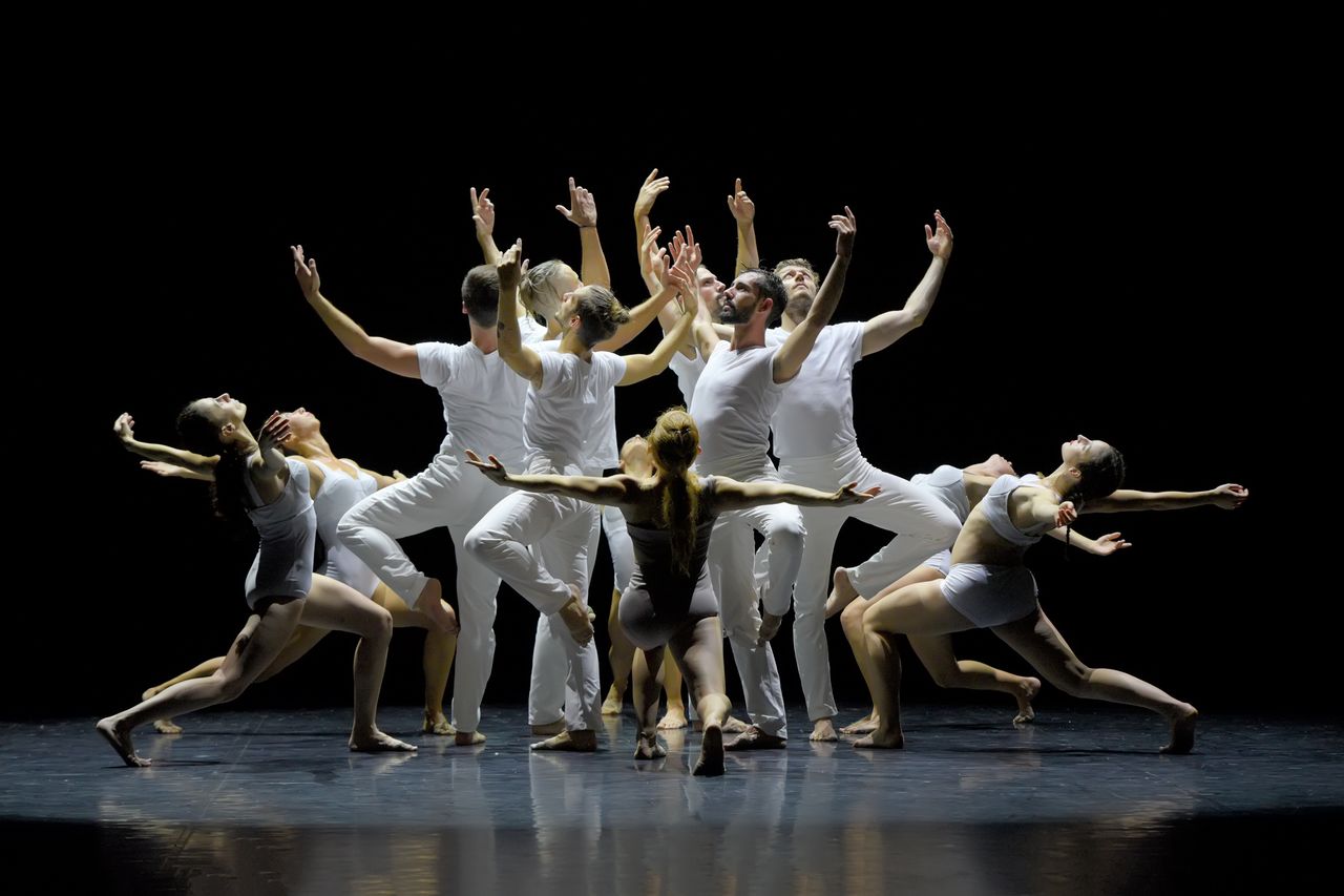 group of dancers in 2 circles. Inner circle arms up, outer circle in a lunge with arms up