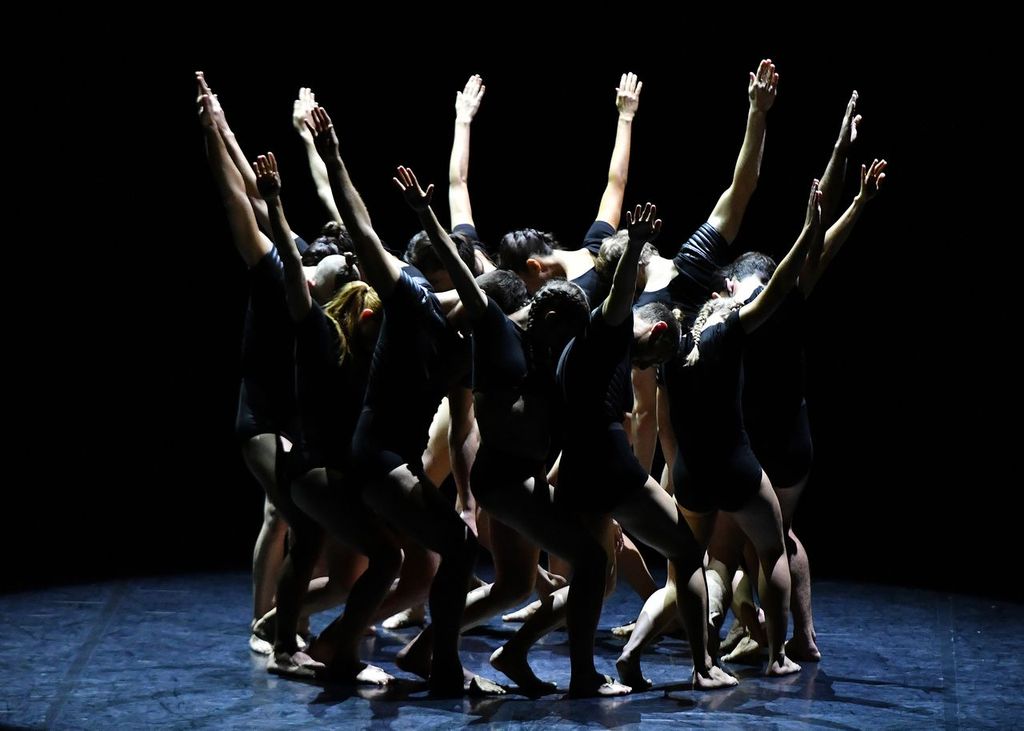 Dancers in a circle, heads resting on shoulder of person in front of them. arms up