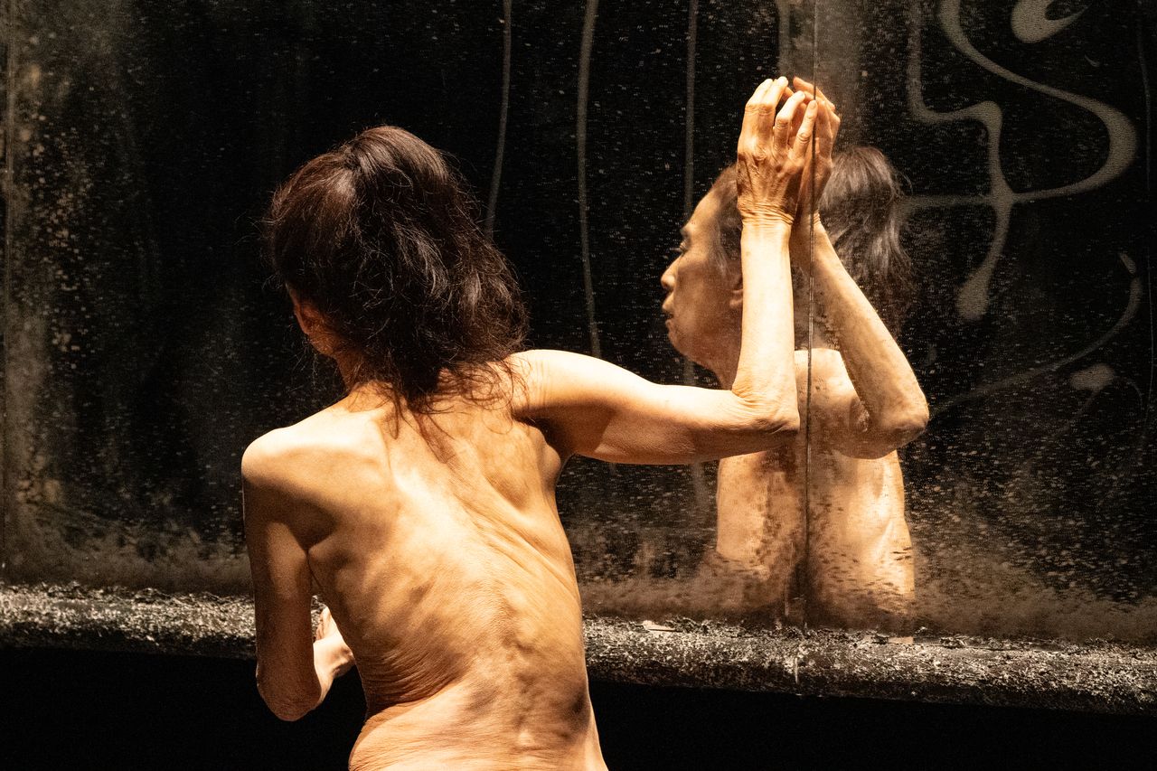 female dancer, naked torso, touches glass of mirror in front of her as she turns her face away