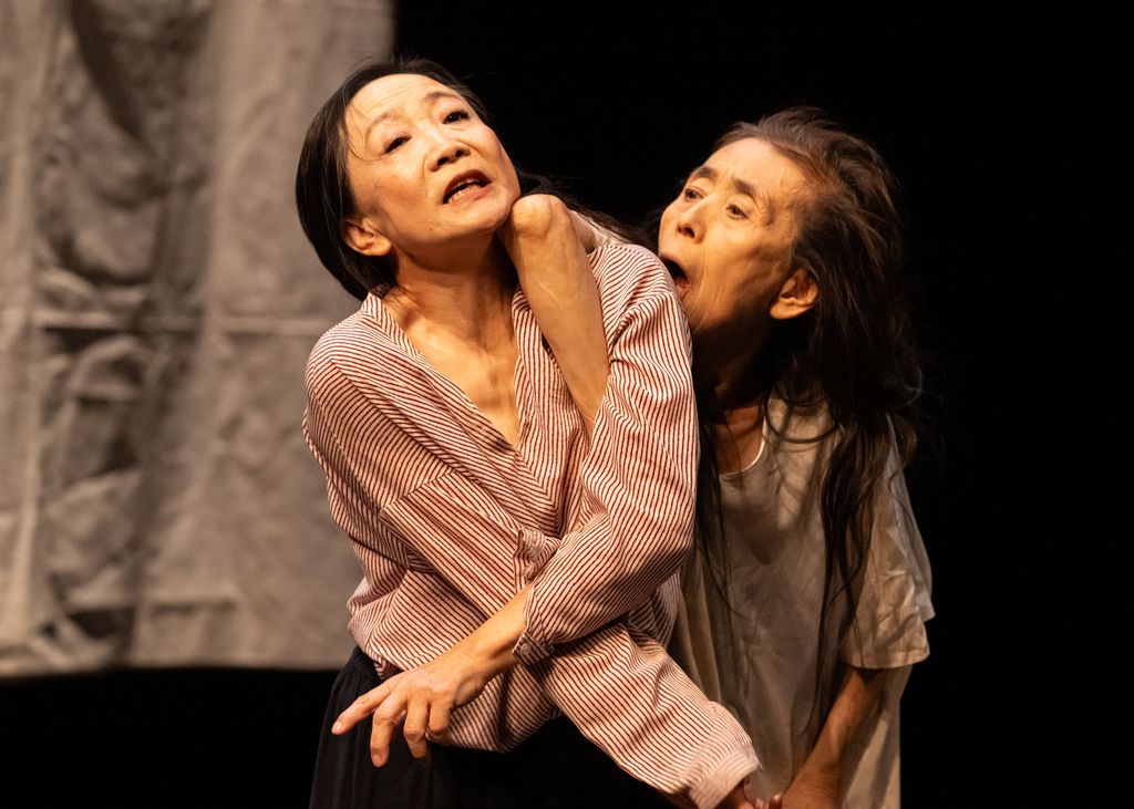 female dancer leaning on shoulder of another looking as if she is trying to bite her arm