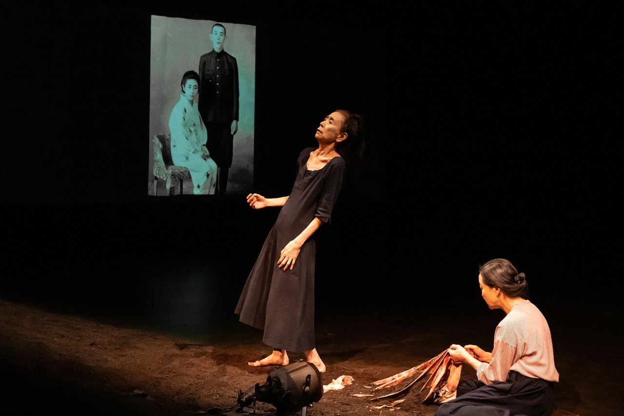 one female dancer standing leaning back, another seated holding a cloth. black and white photo of a man and a woman in background