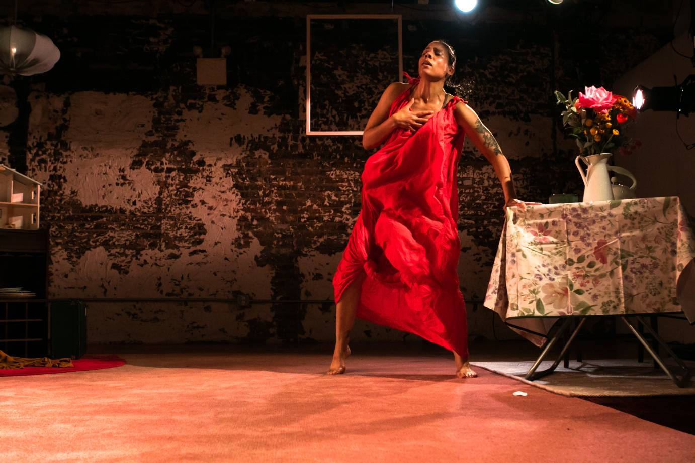 woman in red dress one hand leaning on table one clutching her chest