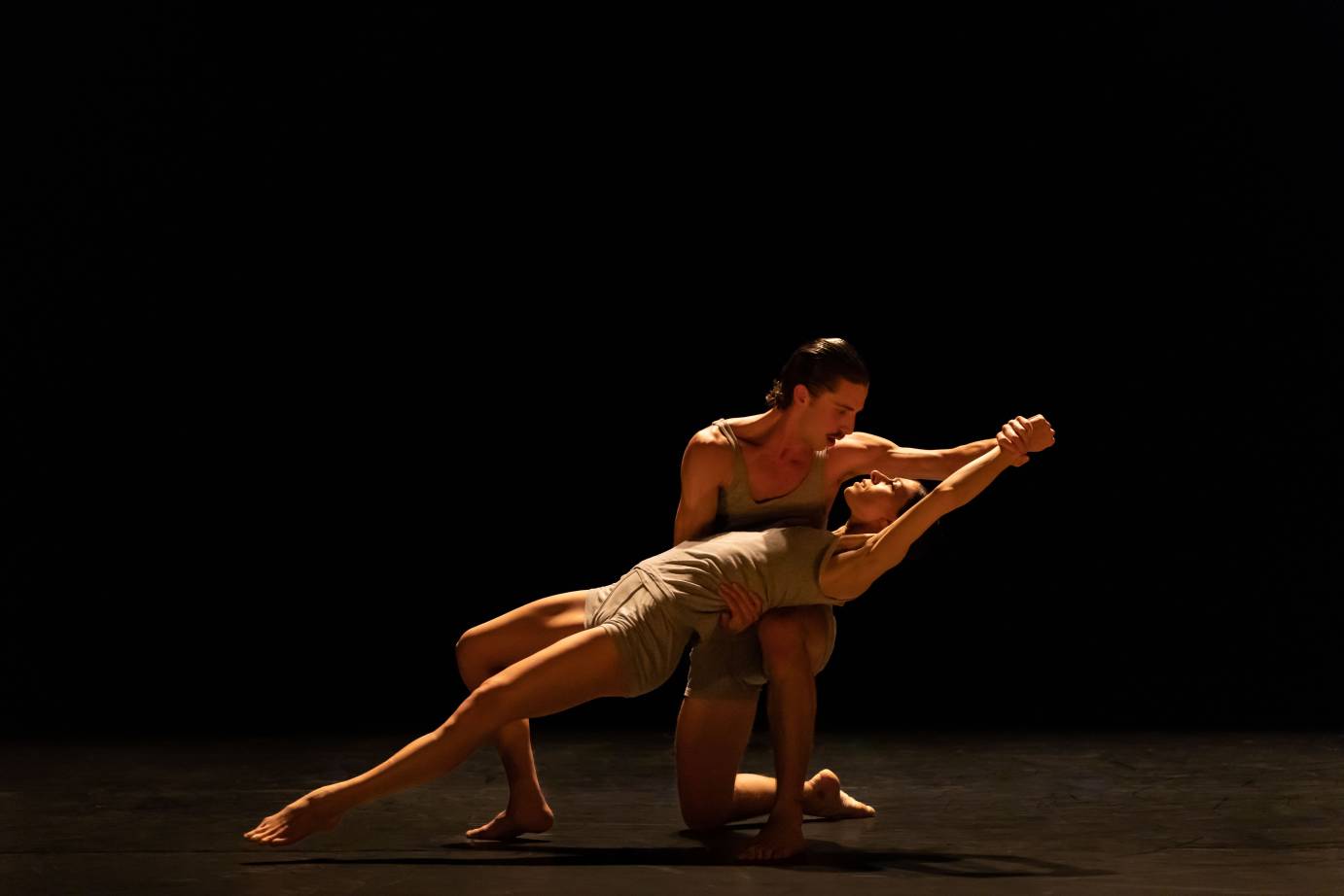 male dancer kneeling. female outstretched over his knees with her body straight. They are holding hands, one hand above her head