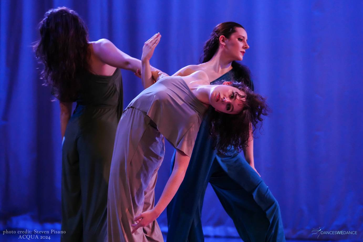3 dancers with arms entwined. Dance closest to audience is held in a back hinge