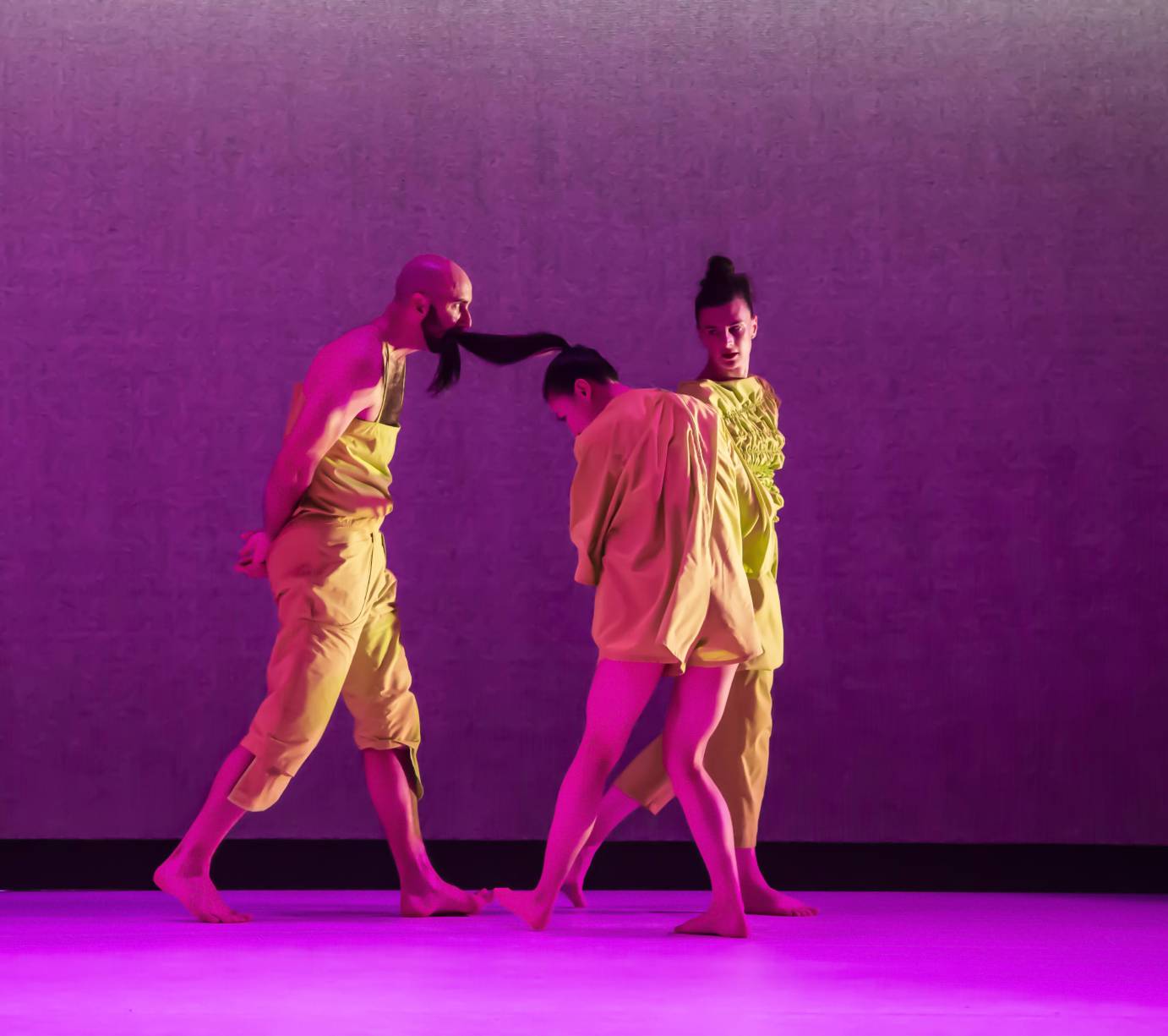 3 dancers close together, one dancer has the pony tail of another in his mouth