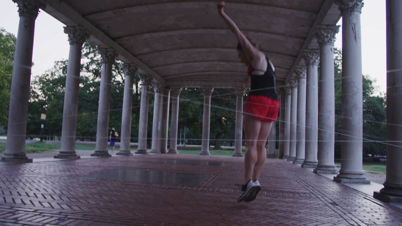 In a Brooklyn park pavilion, Belinda Mcguire jumps into the air, her arms stretched overhead