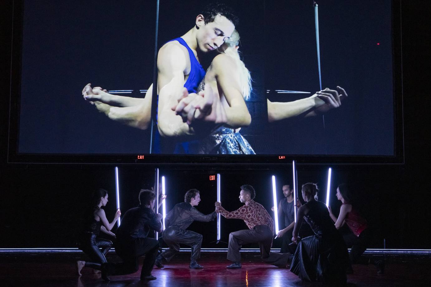 On film, Romeo and Juliet press their hands together in a mirrored room. Bodies close, their hands and arms are bent at the elbow, close to the body. Their heads lean in. Stick bearers are seen below in deep 2nd position. 