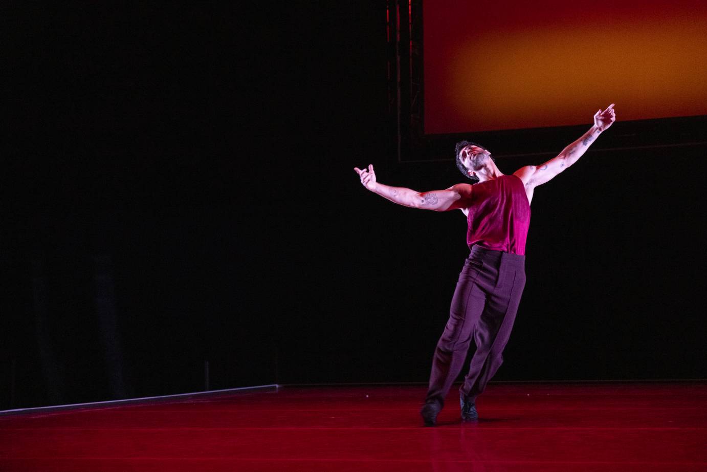 A man on his toes stretches upward as his arms open on the horizontal and his head is thrown back.