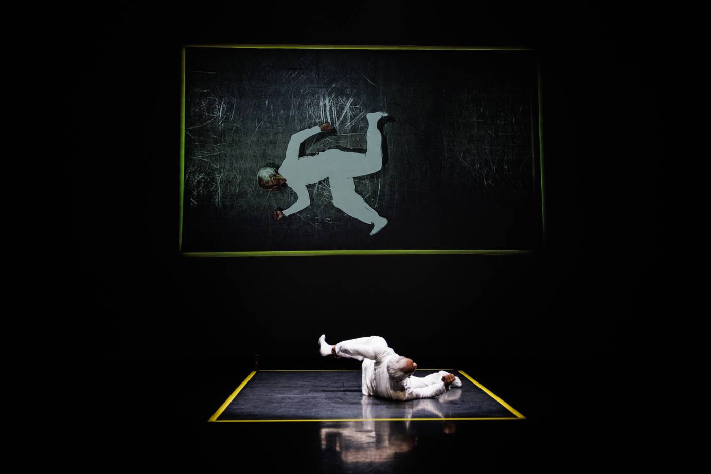 A reflection of a white-costumed, white-haired man in a running position framed in a yellow rectangle.