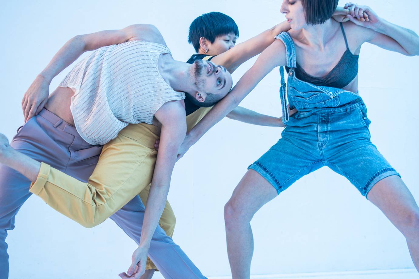 Three dancers interlock hands and lean on each other