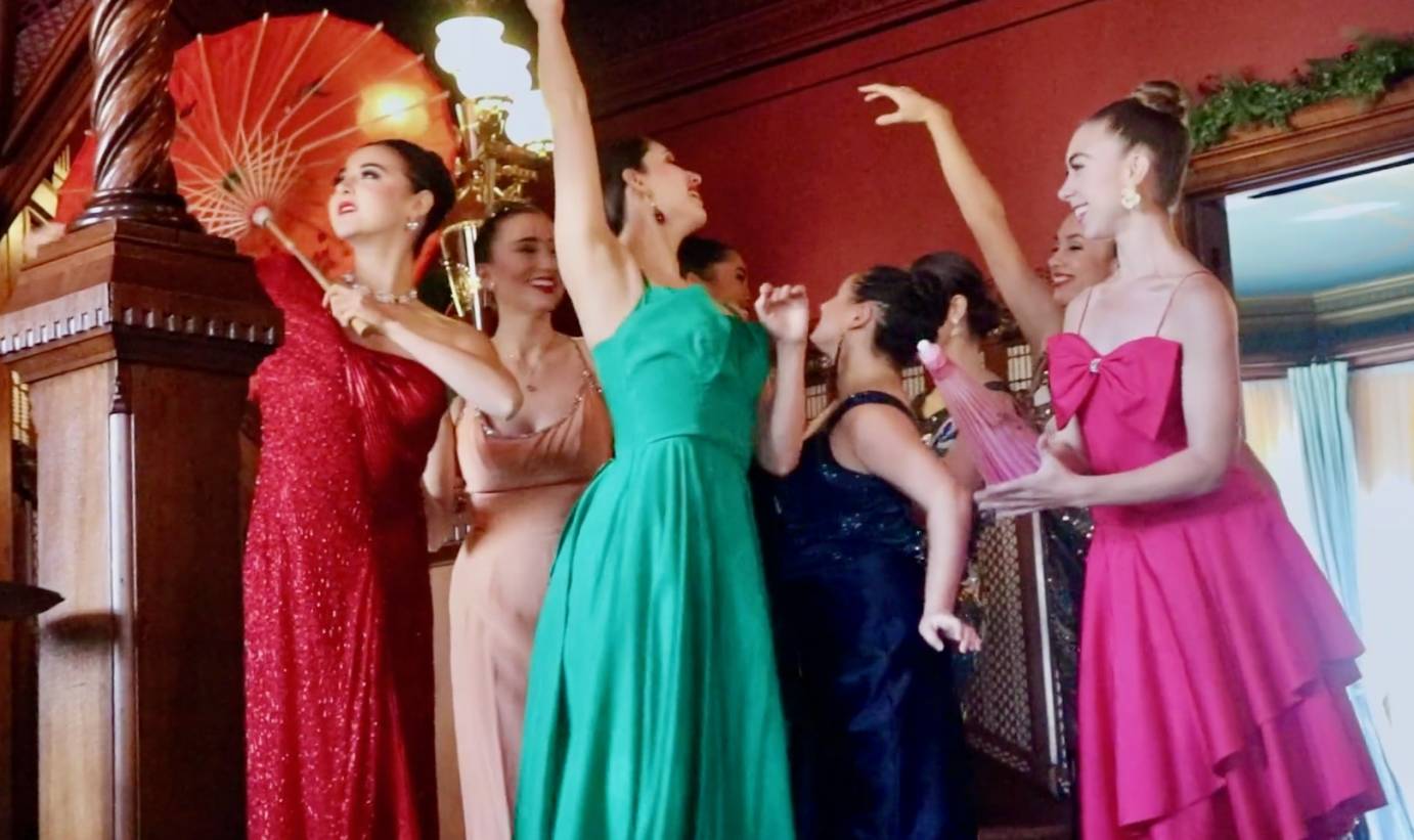 4 women pose in front of a fireplace wearing glittering costumes reminiscent of  flappers and 40's sirens