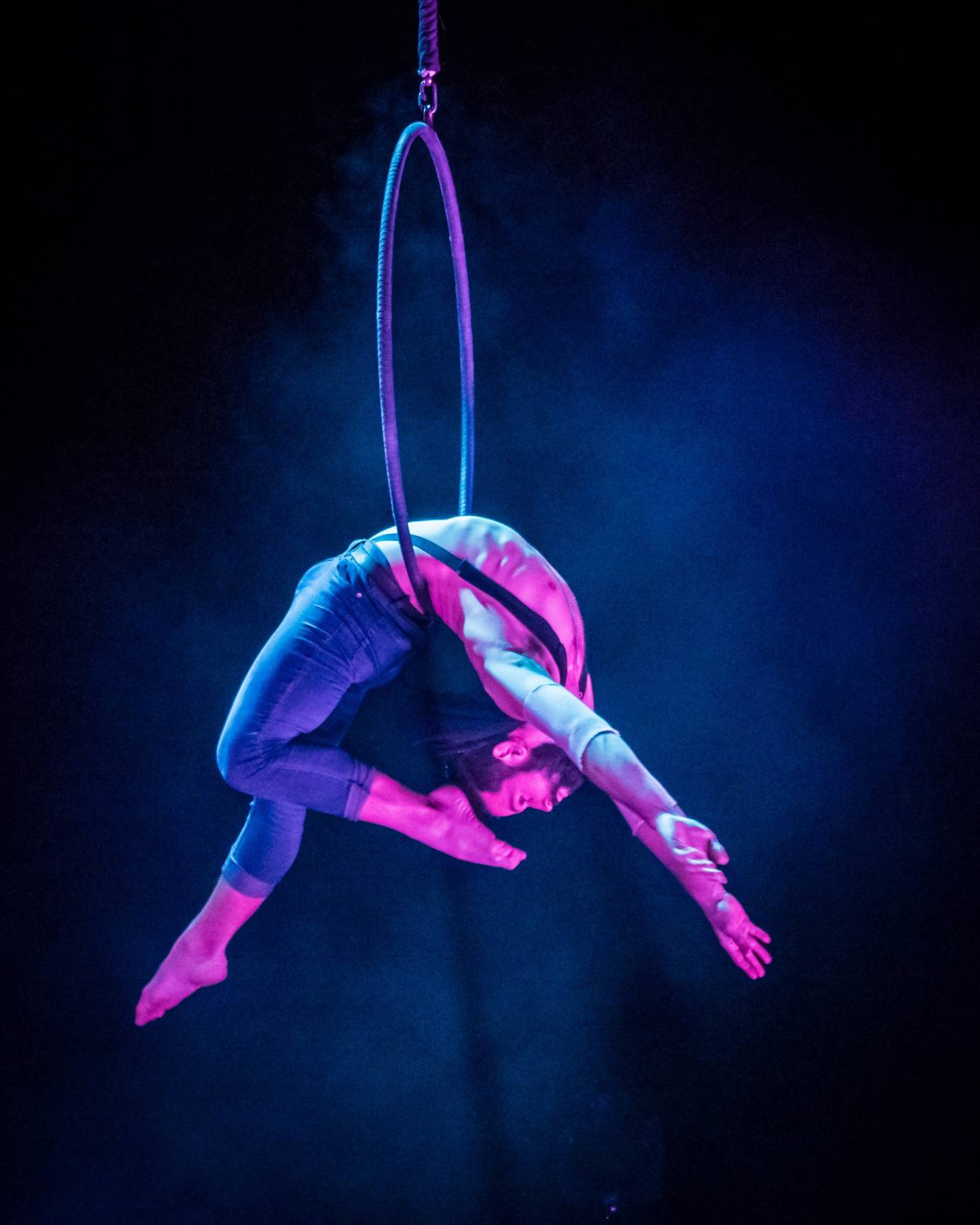 Man with pointed feet hangs from aerial hoop