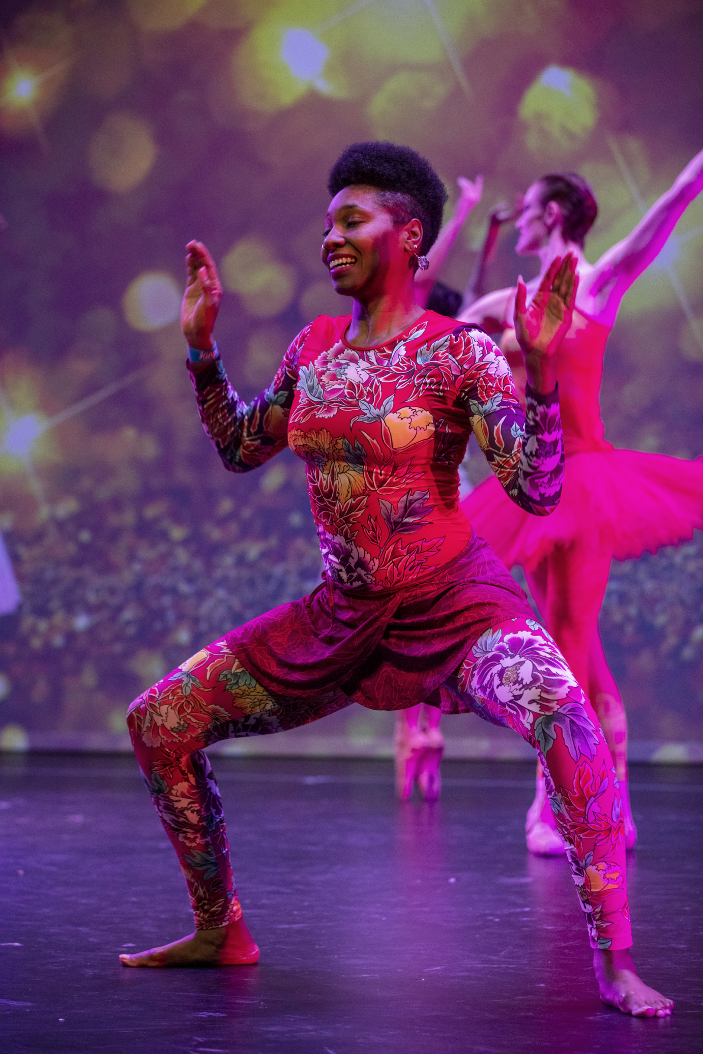 An African dancer performs a deep knee bend in front of a tutu clad dancer en pointe