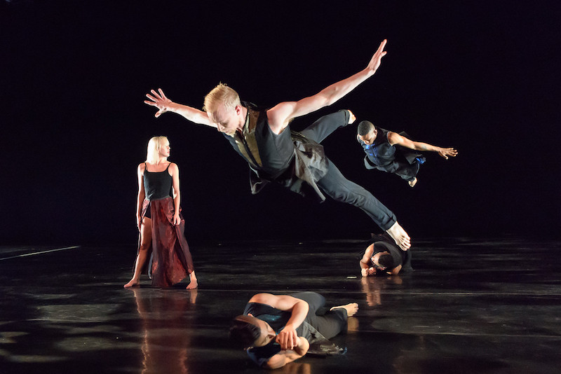 A group of dancers huddle en masse reaching to the wings.