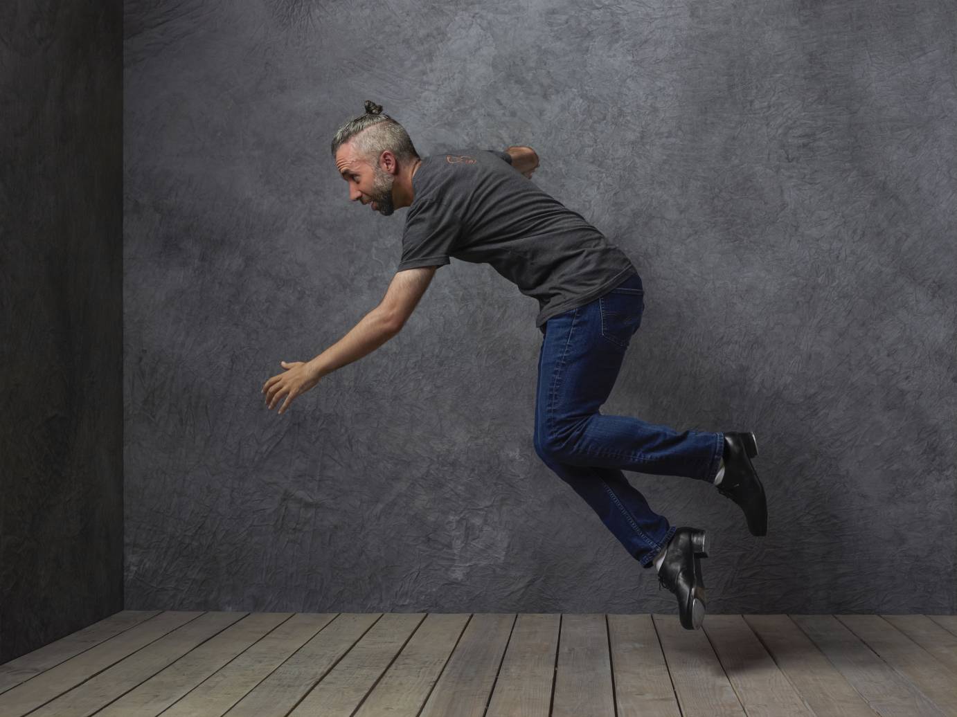 A man with gray hair in a bun tap dances