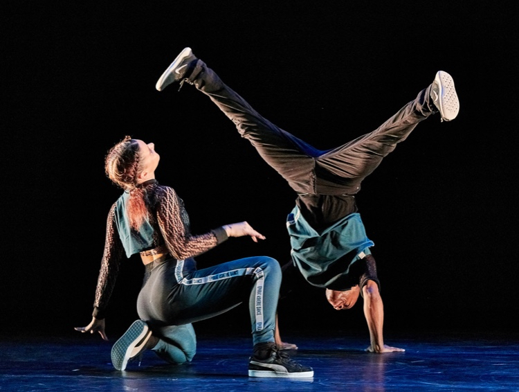 A girl looks up at a man on his hands in a b-boy stance