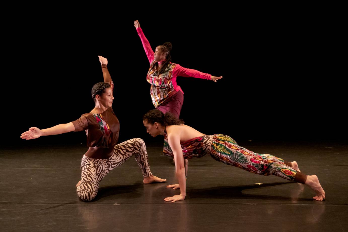 Two women make an obtuse angle with their arms while another planks