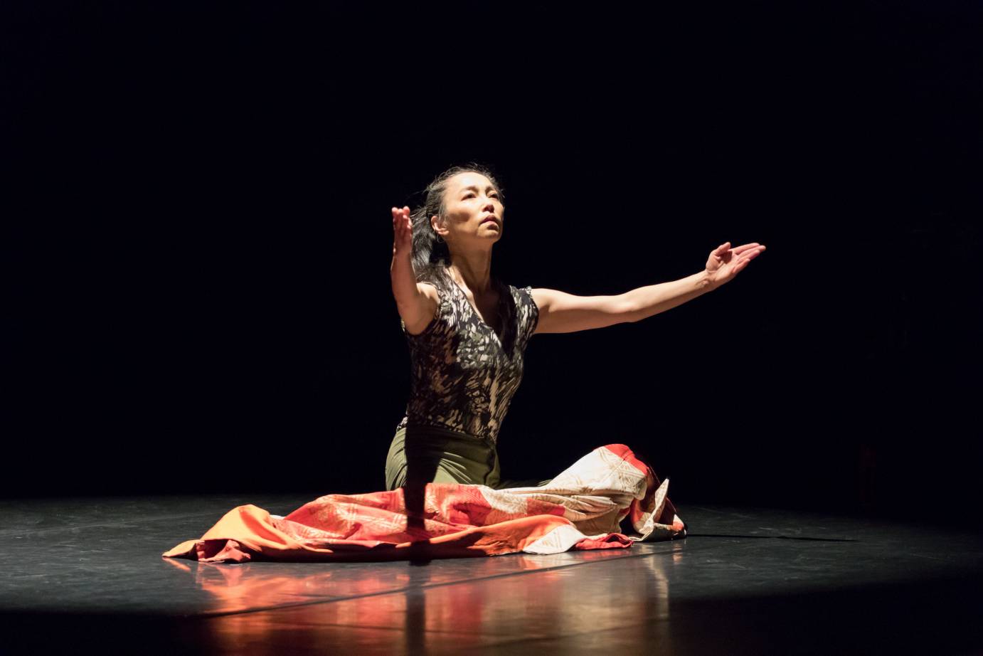 A sitting woman gestures, a red blanket in her lap