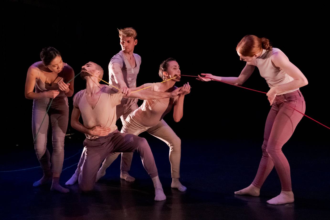 Five dancers hold a colorful string with their hands and mouths