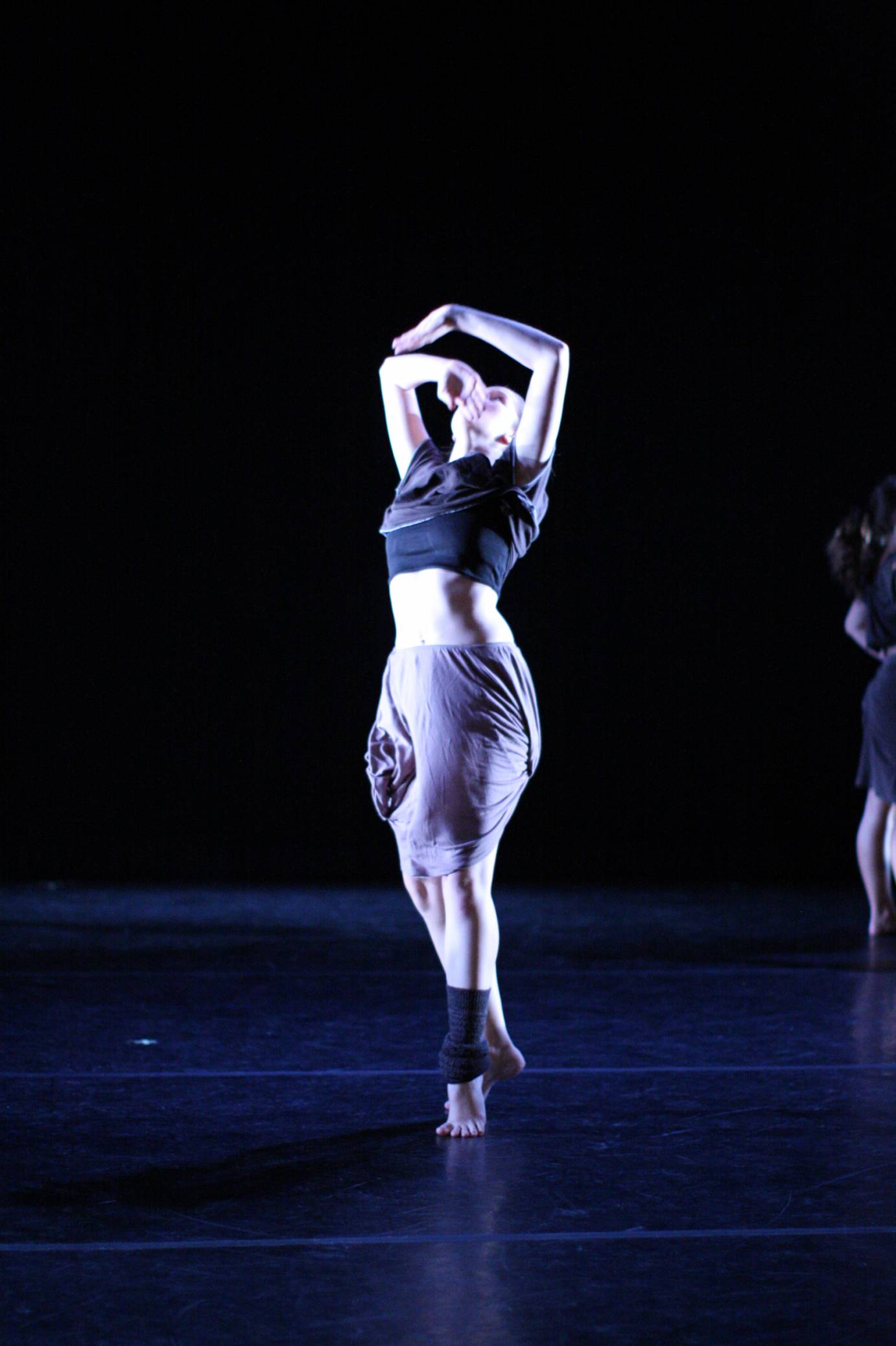 Carissa Landes in a black top and scrunched up skirt, drapes her arms over her head in a piece by Kyle Abraham